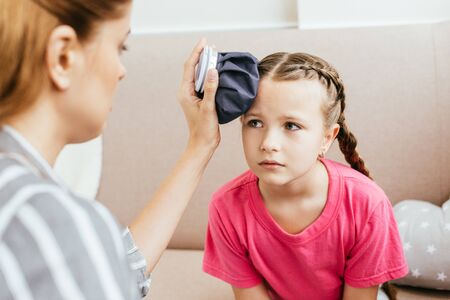 mom holding ice bag compress on head of sad daughter with headache