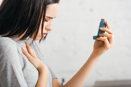 Side view of illness girl holding inhaler at homeの写真素材