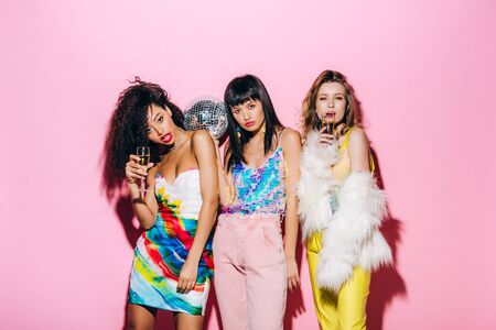 sexy multicultural girlfriends with champagne and disco ball posing on pinkの写真素材