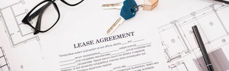 panoramic shot of document with lease agreement lettering near glasses, blueprints and keys on deskの写真素材