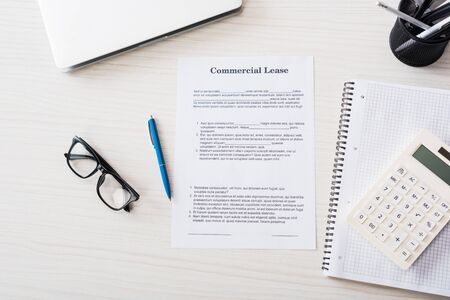top view of document with commercial lease lettering, pen, calculator, laptop and glasses near...