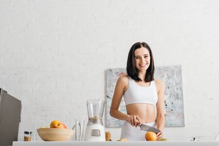 Low angle view of fit sportswoman smiling at camera while preparing smoothie in kitchenの写真素材