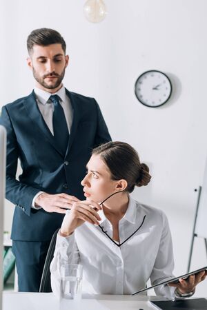 handsome businessman in suit touching shocked businesswoman in officeの写真素材