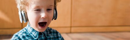 panoramic shot of tired kid yawning while listening music in wireless headphonesの写真素材