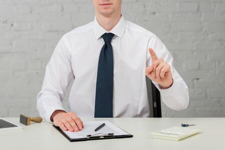 cropped view of realtor in suit pointing with finger while sitting at desk on white, leasing conceptの写真素材