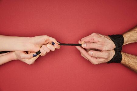 cropped view of woman holding rope on tied male hands isolated on red