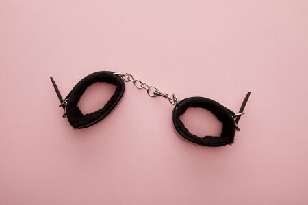 top view of black handcuffs on pink background