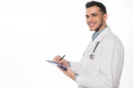 Side view of smiling doctor with clipboard looking at camera isolated on whiteの写真素材