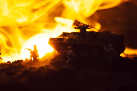 Toy soldiers with tank, fire and sunset on black background, battle scene