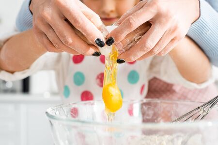 Selective focus of mother and daughter hands breaking egg over bowl together