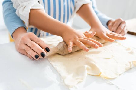 cropped view of mother and daughter rolling dough on tableの写真素材