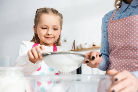 cropped view of mother holding sieve and smiling daughter sifting flour