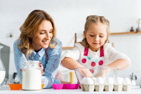 smiling mother looking at daughter cooking dough for pastry