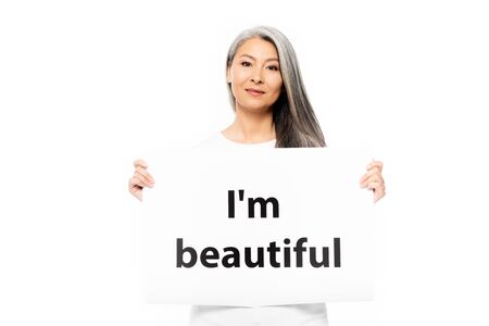 cheerful asian woman holding placard with i`m beautiful lettering isolated on whiteの写真素材