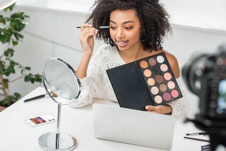 KYIV, UKRAINE - DECEMBER 10, 2019: selective focus of african american influencer in braces applying eye shadow near smartphone with soundcloud app on screenのeditorial素材