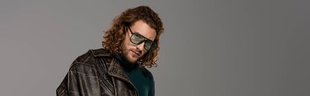panoramic shot of handsome man in leather jacket looking at camera isolated on grey