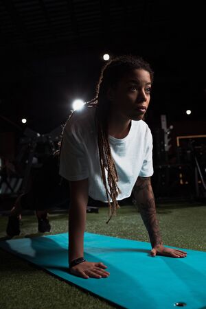 African american woman standing in plank on fitness mat in gymの写真素材