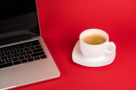 Laptop with blank screen and coffee cup on saucer on red backgroundの写真素材