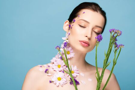 young woman with closed eyes near blooming flowers isolated on blueの写真素材