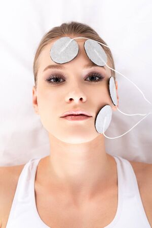 Top view of attractive girl looking at camera during facial electrotherapy on massage couch