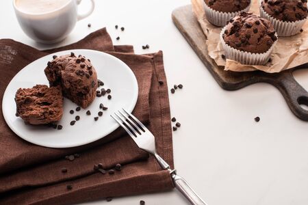 fresh chocolate muffins on wooden cutting board near plate with fork and coffeeの写真素材