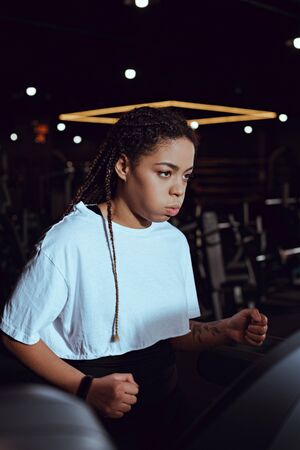 Selective focus of african american woman puffing out cheeks while running on treadmill