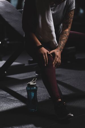 cropped view of tattooed african american girl touching knee in gym