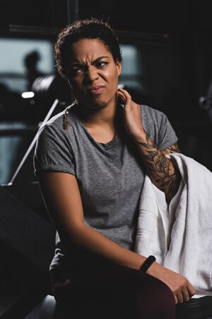 displeased african american girl with tattoo touching neckの写真素材