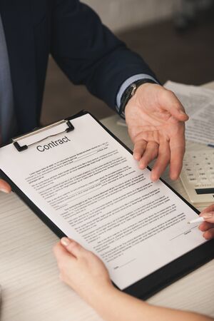 cropped view of agent pointing with hand at clipboard with contract lettering near woman with pen
