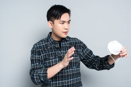 young asian man showing refuse gesture while holding respirator mask on grey backgroundの写真素材