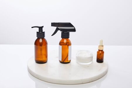 Dispenser bottles of oil and cosmetic cream on round stand isolated on greyの写真素材