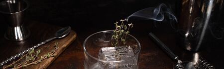 transparent glass with burning herb with smoke and ice cube on wooden surface, panoramic shotの写真素材