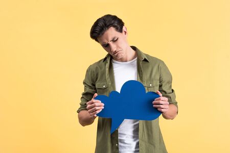 skeptical man holding blue cloud speech bubble, isolated on yellowの写真素材