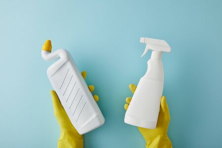 cropped view of housekeeper in rubber gloves holding spray bottle and bottle with toilet cleaner on...
