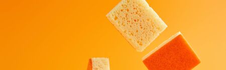 panoramic shot of yellow falling sponges for house cleaning isolated on orangeの写真素材