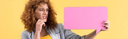 panoramic shot of frightened girl looking at empty pink speech bubble, isolated on yellowの写真素材