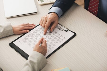 cropped view of realtor pointing with finger at clipboard with contract lettering near clientの写真素材