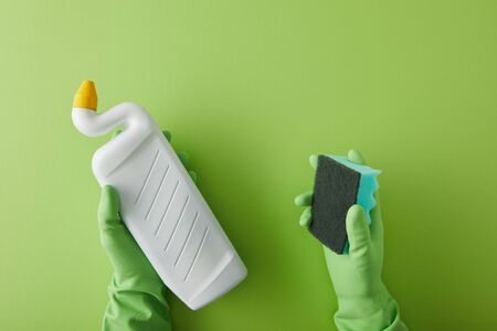 cropped view of housekeeper in rubber gloves holding sponge and bottle with toilet cleaner on greenの写真素材