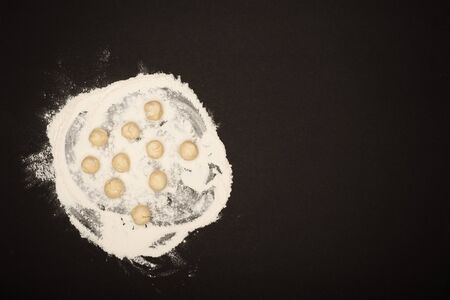 top view of raw dough balls for dumplings on flour on black backgroundの写真素材
