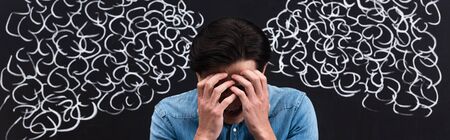 panoramic shot of frustrated young man with steam drawing on chalkboard behind