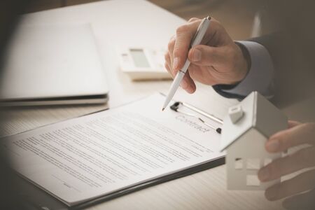 cropped view of agent holding pen and touching house model near clipboard with contract letteringの写真素材