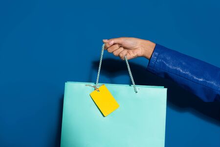 cropped view of african american woman holding shopping bag with blank label on blueの写真素材