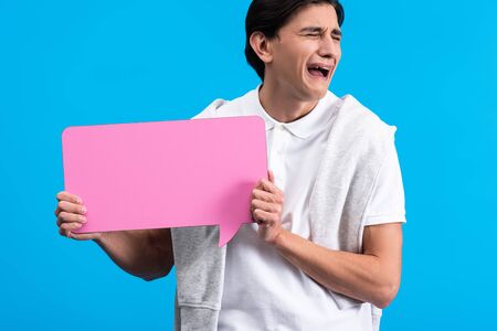 crying man holding pink speech bubble, isolated on blue