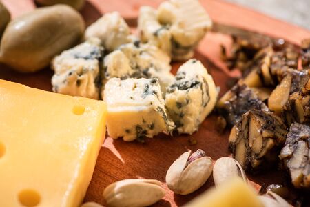 Selective focus of pieces of cheese, pistachios and olive on wooden background