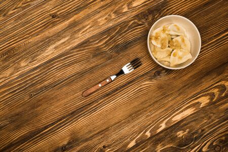 top view of delicious varenyky with fried onion in bowl on wooden table with fork