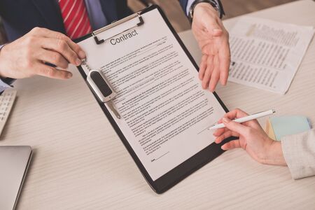 cropped view of agent pointing with hand at clipboard with contract lettering and car key near...