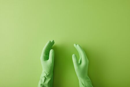 cropped view of hands of housekeeper in rubber gloves on green