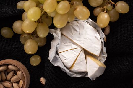 Top view of pieces of camembert with grapes and bowl of pistachios isolated on blackの写真素材