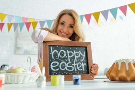 selective focus of cheerful woman holding chalkboard with happy easter letteringの写真素材