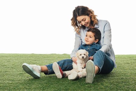 smiling mother holding Havanese puppy and looking at son isolated on whiteの写真素材